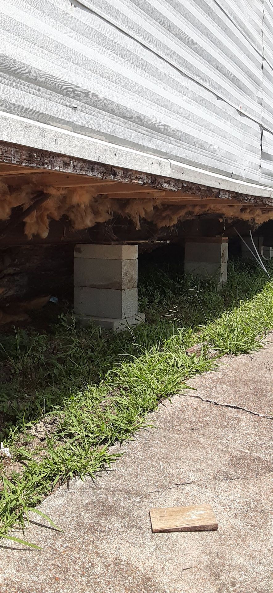 Underneath view of a structure supported by concrete blocks on a grassy surface, showing exposed insulation.